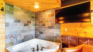 A bathroom with a stone mosaic wall, a white bathtub, wooden cabinets, and a leather chair.