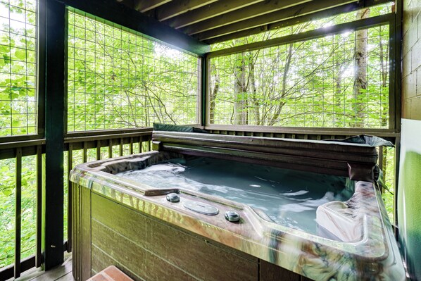 A hot tub with a view of a forest through a window.