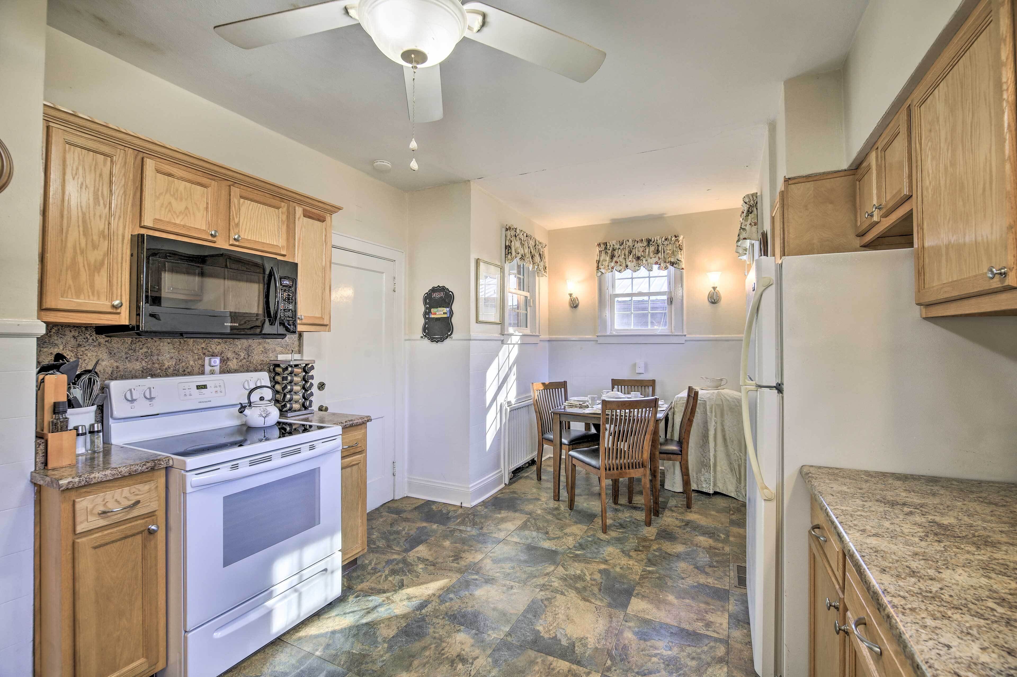 A kitchen with wooden cabinets, a microwave, stove, and a dining area with chairs and a table.