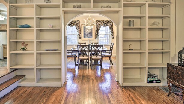 Un espace repas avec une table et des chaises en bois, entouré d’étagères blanches où sont disposés divers objets.