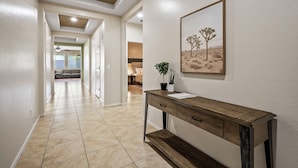 Un couloir avec une console en bois, un tableau représentant un paysage désertique encadré et une plante en pot.