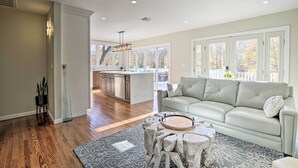 A spacious living room with a grey sofa, a coffee table, and a kitchen in the background. - Updated Getaway w/ Pool & Hot Tub on < 3 Acres! (Stony Point)