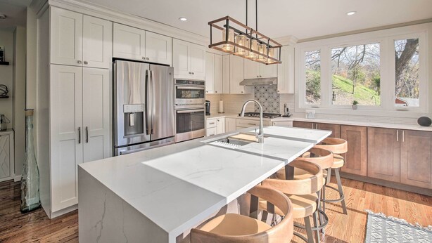 A modern kitchen with white cabinetry, stainless steel appliances, a large island with bar stools, and a view of the outdoors through large windows. - Updated Getaway w/ Pool & Hot Tub on < 3 Acres! (Stony Point)