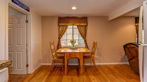 Un comedor con una mesa y sillas de madera, una ventana con cortinas y un letrero sobre la puerta.
