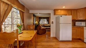 Una cocina con armarios de madera, un refrigerador y una zona de comedor con mesa y sillas.