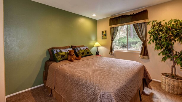 Un dormitorio con una cama grande, una mesita de noche, una lámpara, una ventana con cortinas y una planta en maceta.
