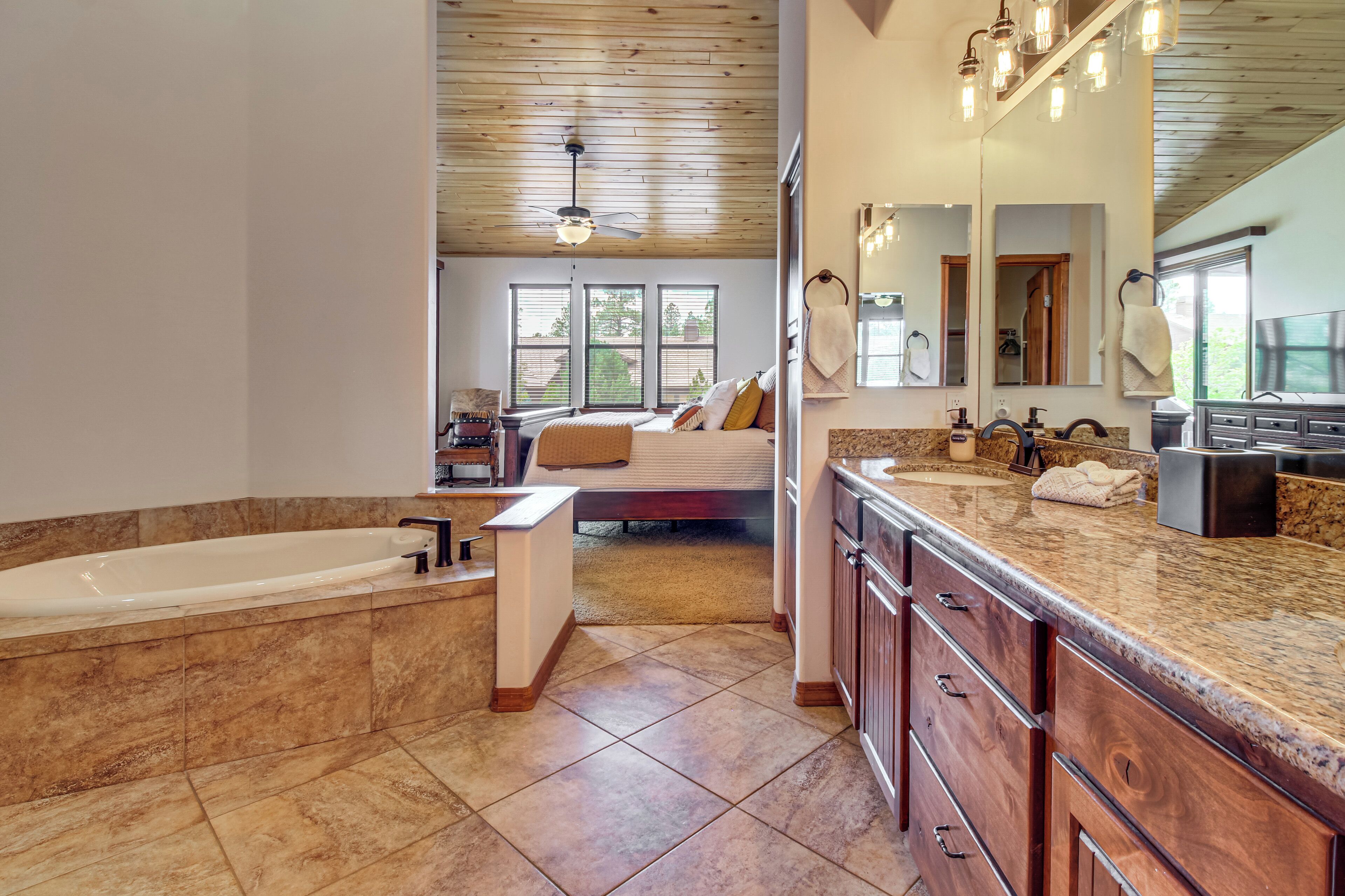 A spacious bathroom with a large bathtub, a vanity with a mirror, and a ceiling fan.