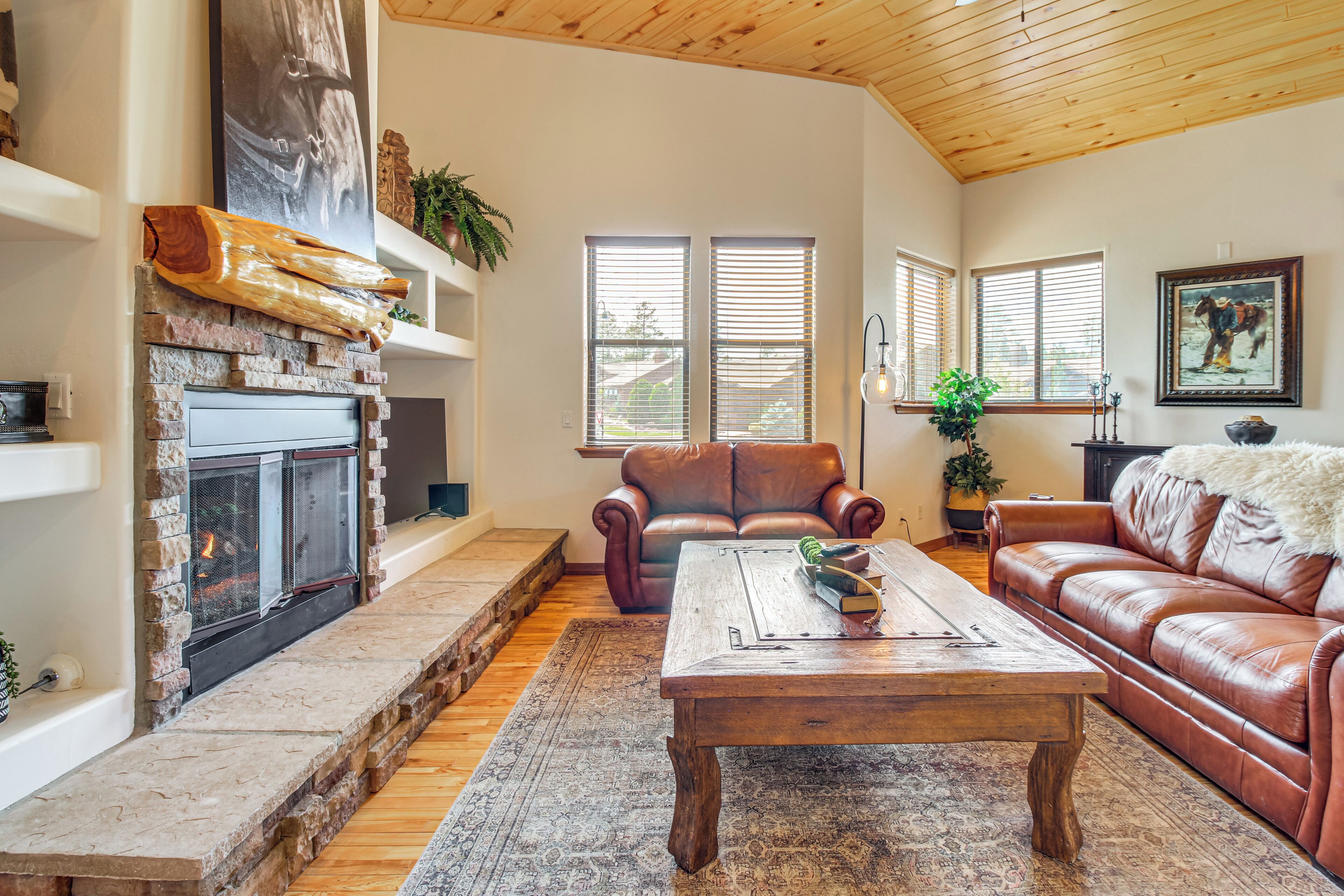 A living room with a fireplace, leather sofas, a coffee table, and large windows.