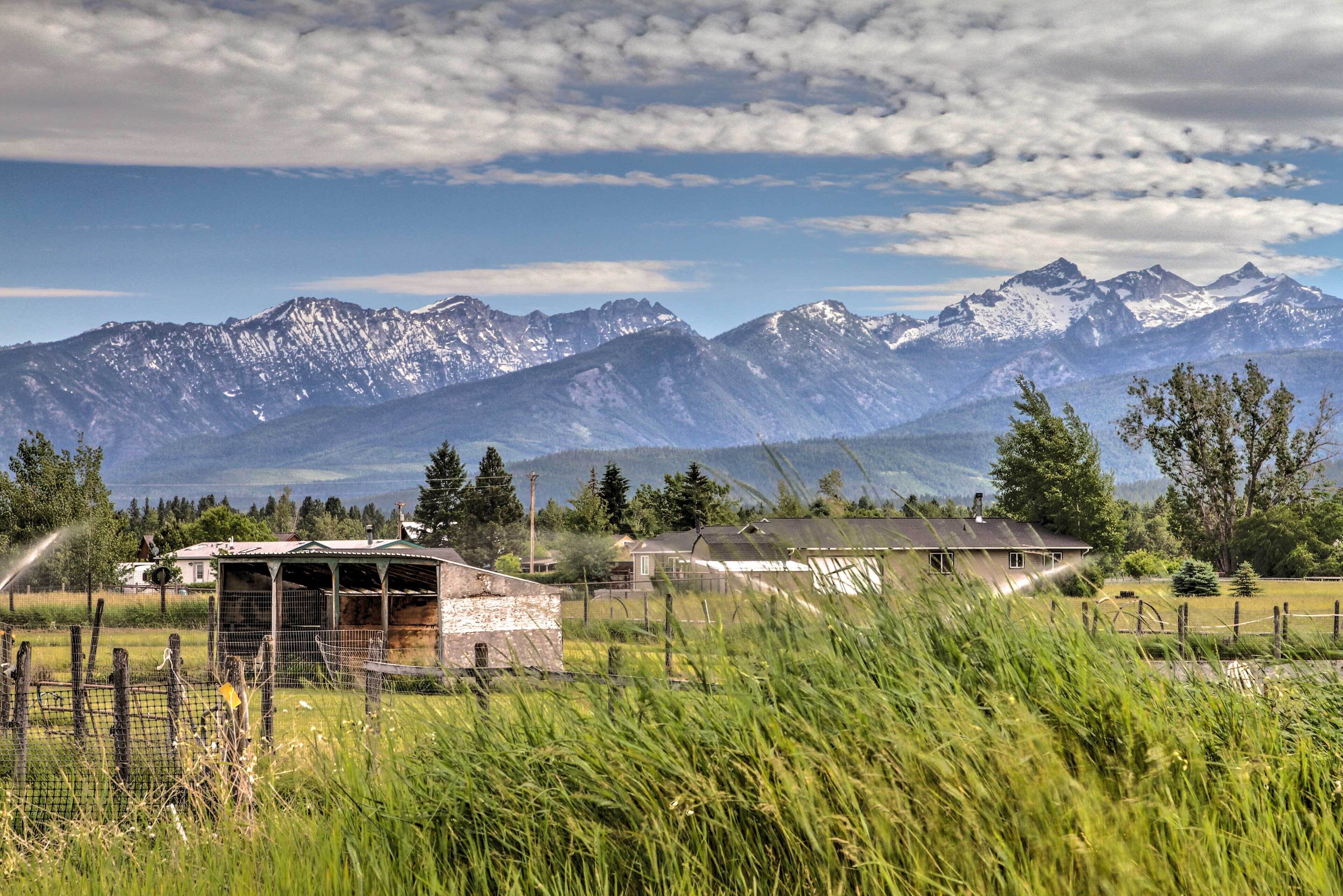 A rural landscape with mountains in the background, a small wooden structure, and a fenced field.