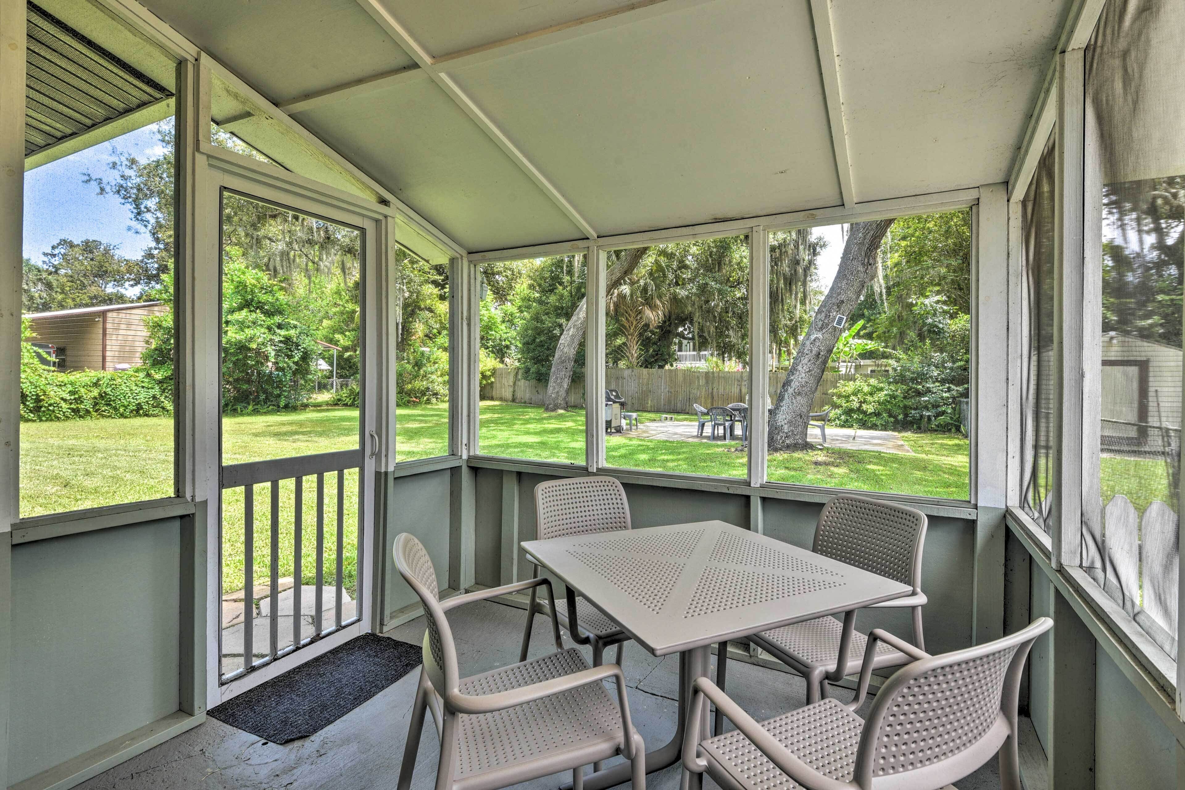 A covered patio with a table and chairs, large windows, and a view of a backyard.