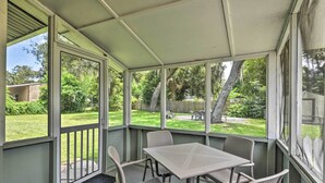 Une terrasse couverte avec une table et des chaises, de grandes fenêtres et une vue sur le jardin arrière.