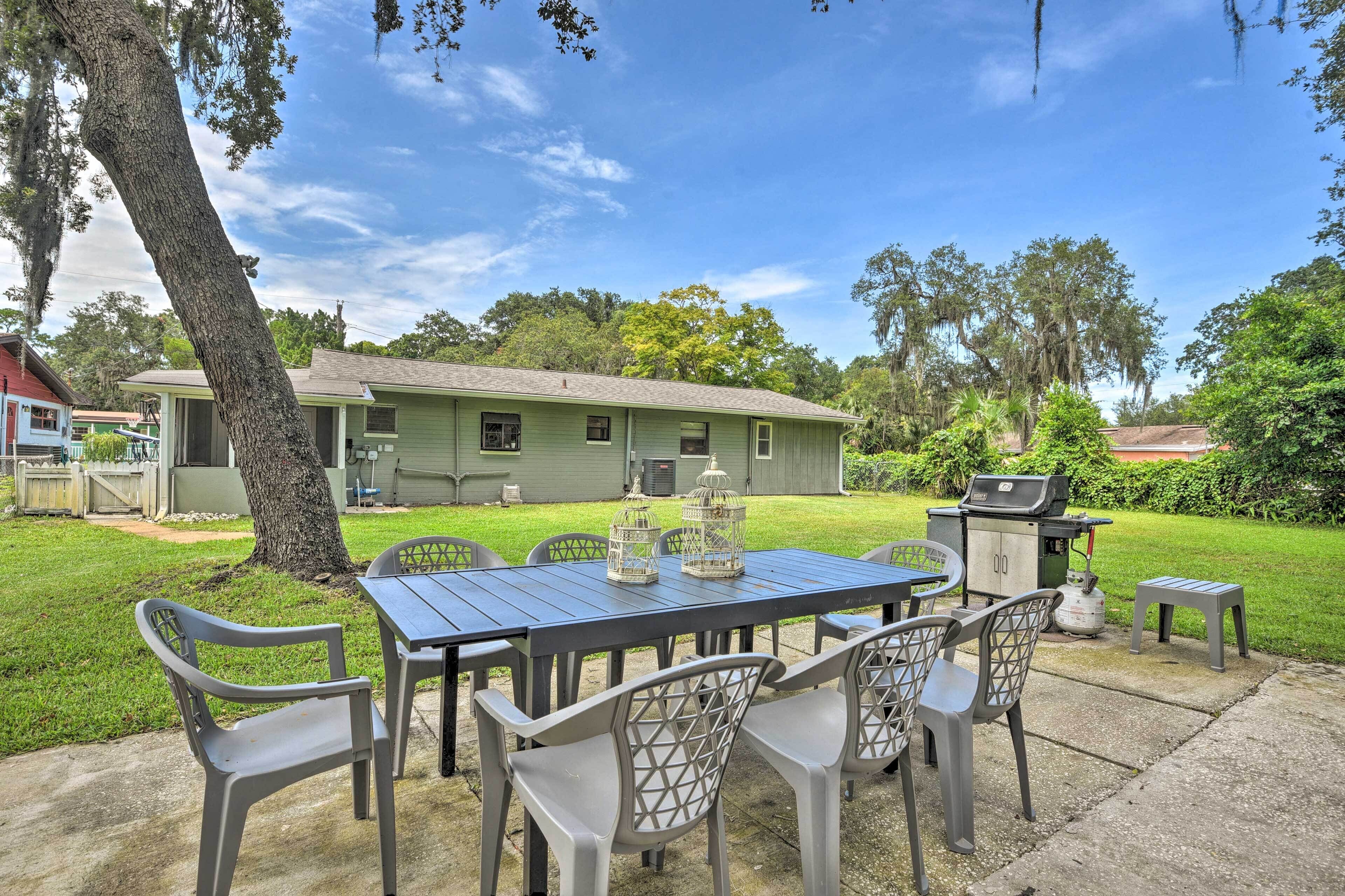 A patio with a table and chairs, a grill, and a small garden area with a house in the background.