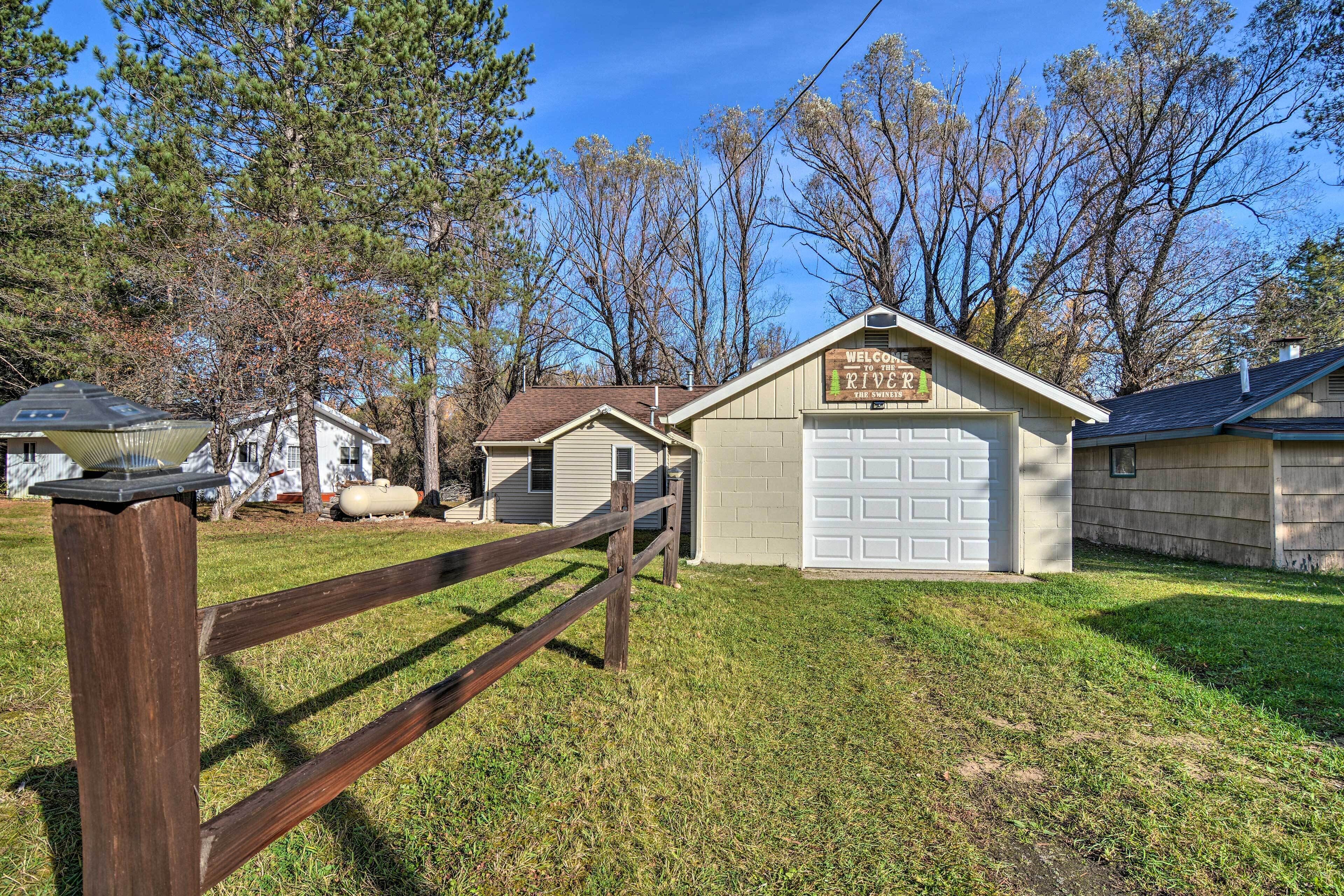 A small building with a garage, surrounded by a wooden fence and trees.