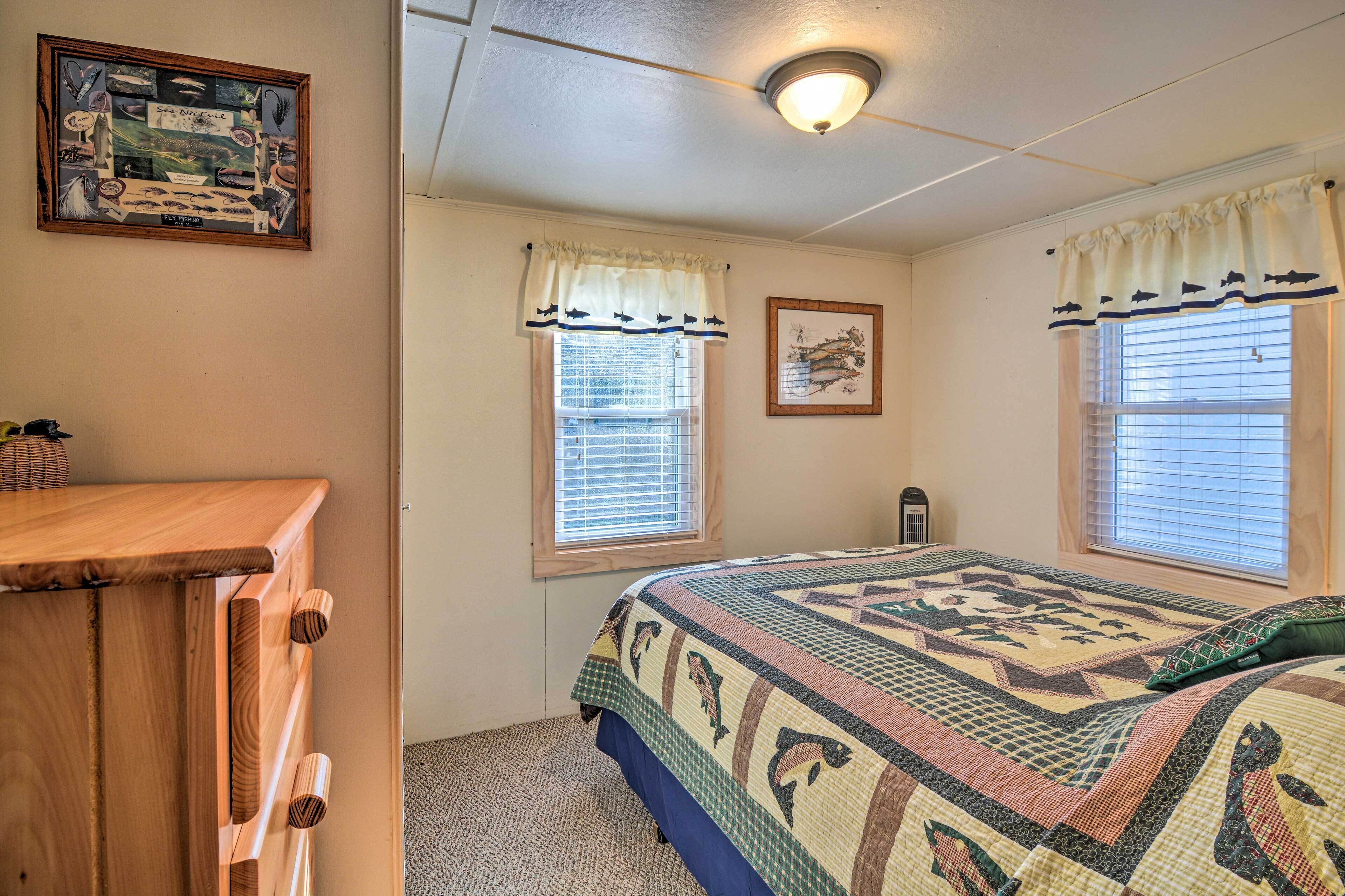 A bedroom with a bed, two windows with curtains, a ceiling light, and a wall-mounted picture.