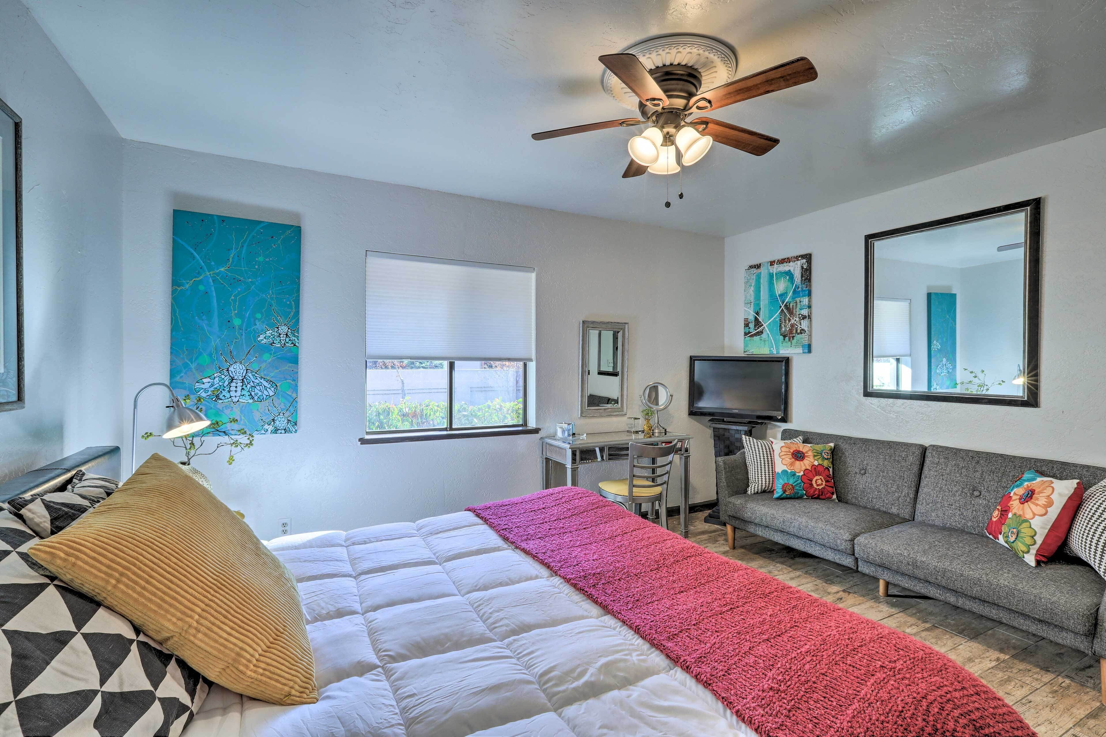A bedroom with a bed, a desk, a sofa, and a ceiling fan.