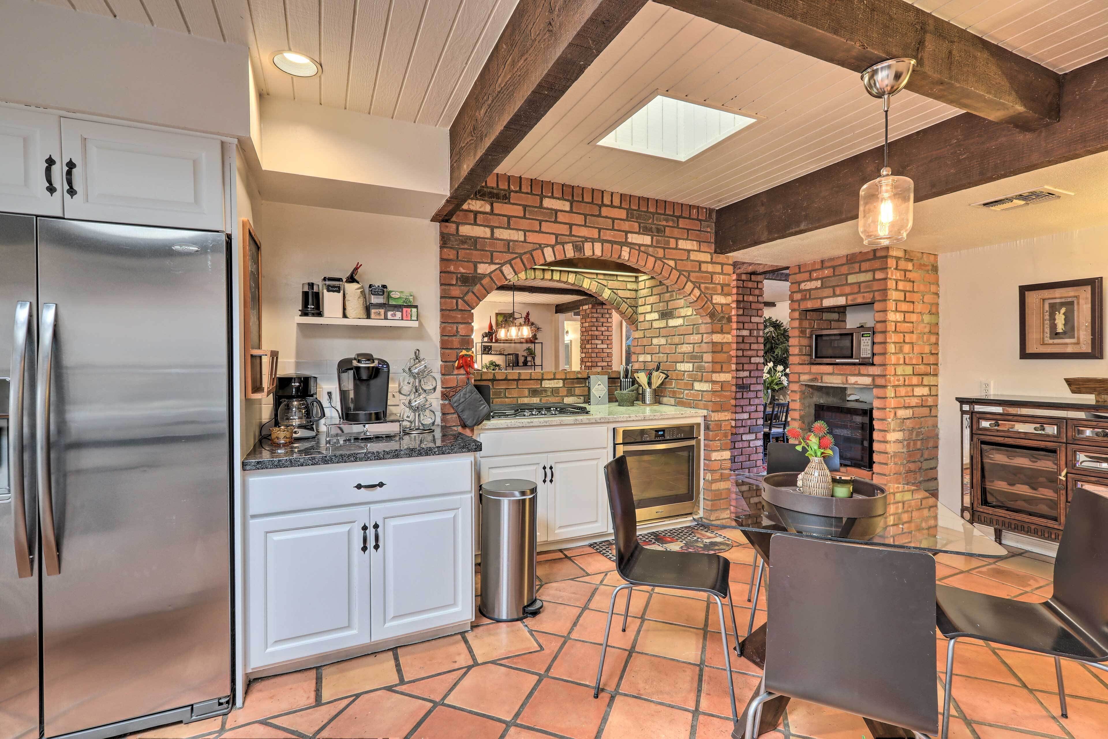 A kitchen with a brick archway, a stainless steel refrigerator, and a dining area with chairs.