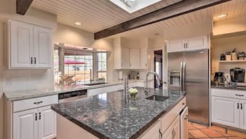 Una cocina moderna con armarios blancos, encimera de granito y refrigerador de acero inoxidable.