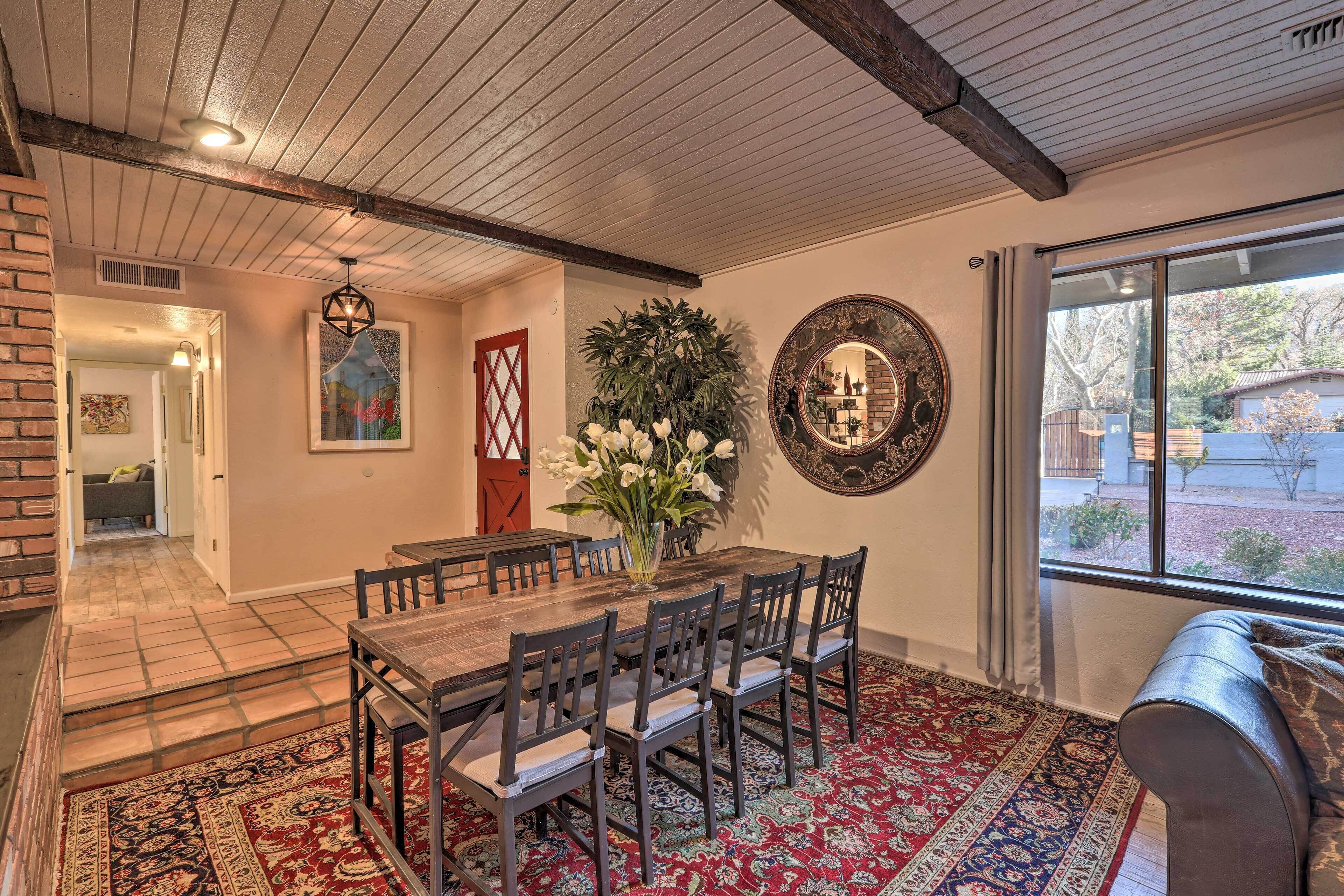 Un comedor con mesa y sillas de madera, un tapete rojo estampado y un ventanal con vistas al exterior.