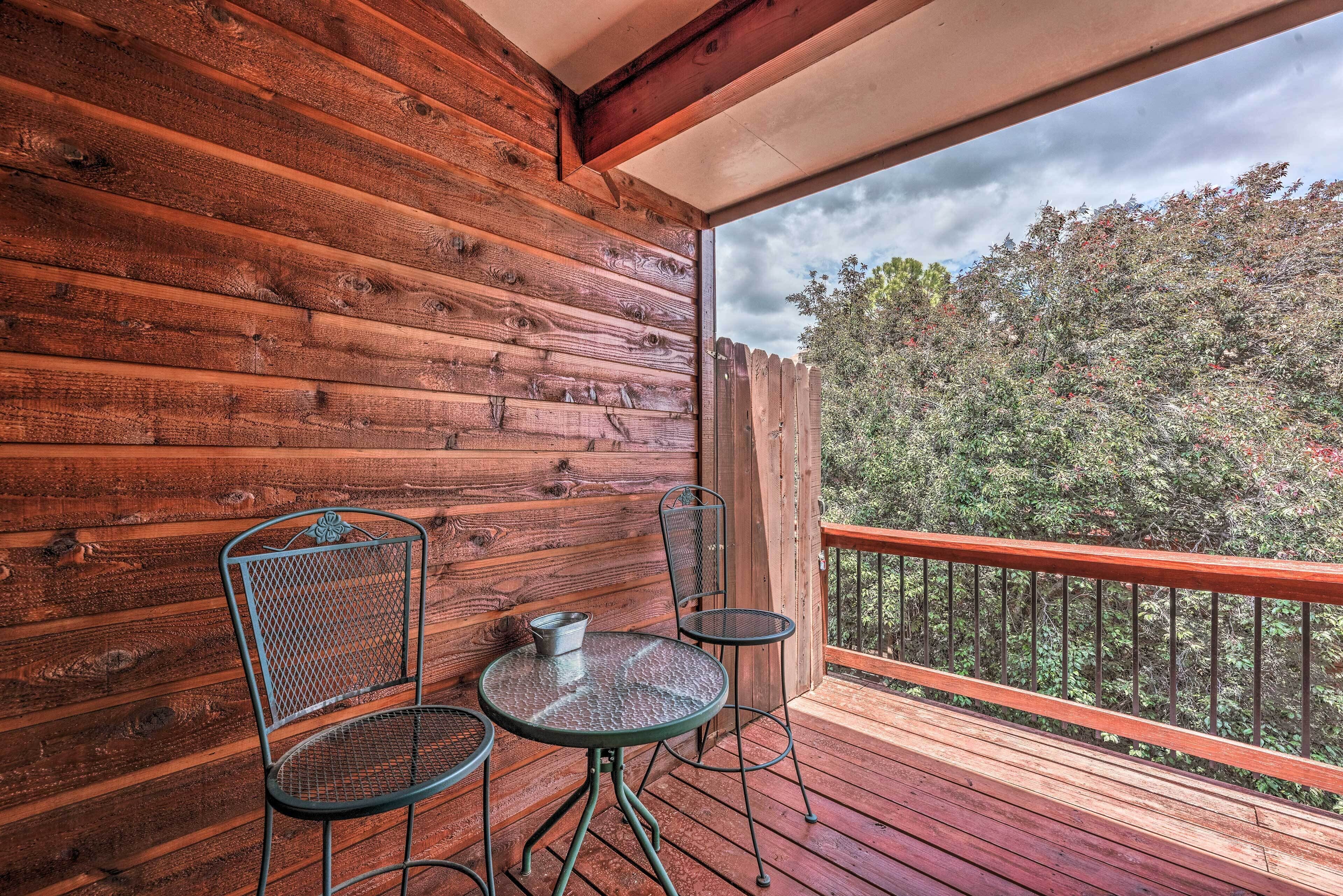 A wooden deck with two metal chairs and a small table, overlooking a forested area.