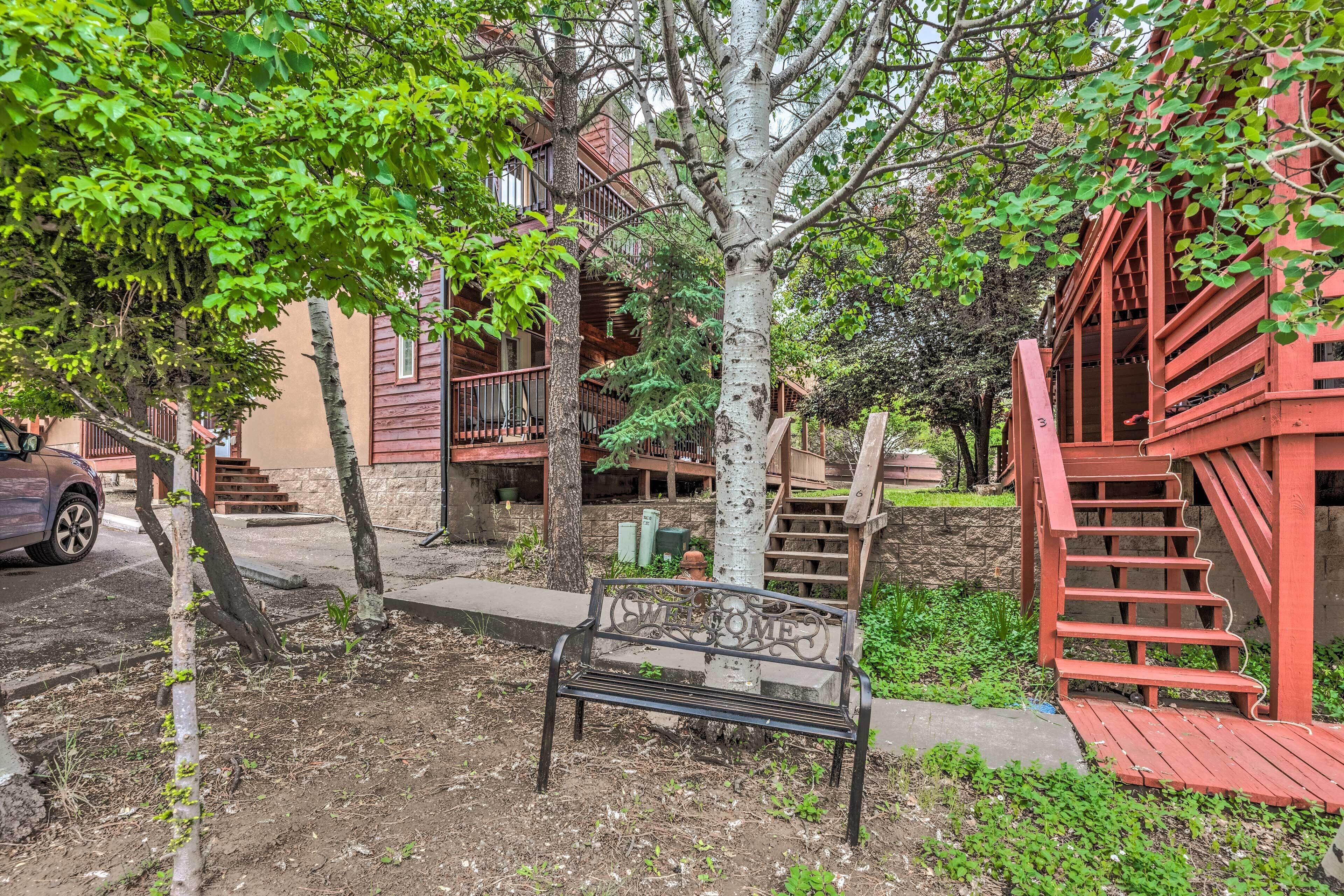 A wooden bench with a "WELCOME" sign in a landscaped area with trees and a red staircase.