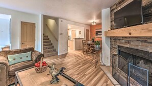 A living room with a fireplace, a dining area, and a staircase leading to an upper level. - Mountain Lodge w/ Hot Tub, Walk to Grindstone Lake (Ruidoso)
