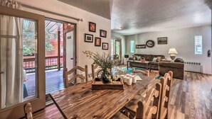 A dining area with a wooden table, chairs, and a vase of flowers. There is a sliding glass door leading to an outdoor patio. - Mountain Lodge w/ Hot Tub, Walk to Grindstone Lake (Ruidoso)
