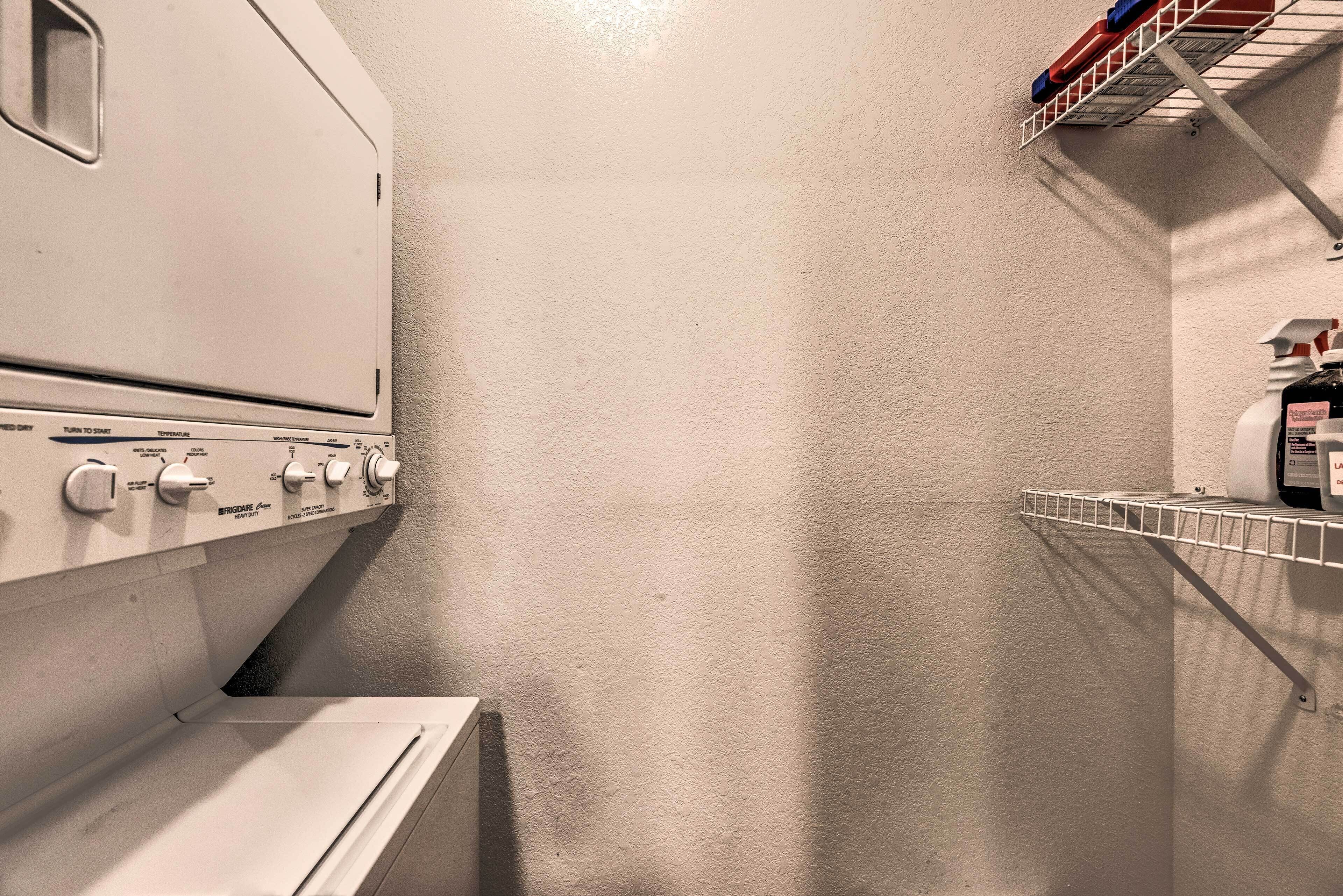A laundry room with a washing machine, dryer, and a metal shelf with bottles.