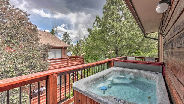 A wooden deck with a hot tub, surrounded by trees and a cloudy sky. - Mountain Lodge w/ Hot Tub, Walk to Grindstone Lake (Ruidoso)