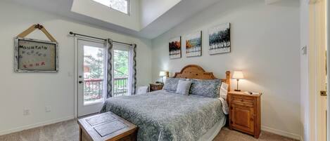 Ein Schlafzimmer mit einem großen Bett, einem Nachttisch aus Holz, einem kleinen Tisch und einem Deckenventilator. An der Wand hängen drei gerahmte Bilder und es gibt ein Fenster mit Vorhängen.
