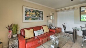 A living room with a red leather sofa, a glass coffee table, and a dining area with a glass table and metal chairs. - Longboat Key Condo W/lanai, Walk to Beach & Shops (Longboat Key)