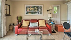 A living room with a red leather sofa, a glass coffee table, a painting of flowers, and a lamp. - Longboat Key Condo W/lanai, Walk to Beach & Shops (Longboat Key)