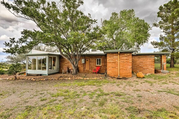 A rustic cabin with a glass-enclosed porch, a brick exterior, and a large tree in front.
