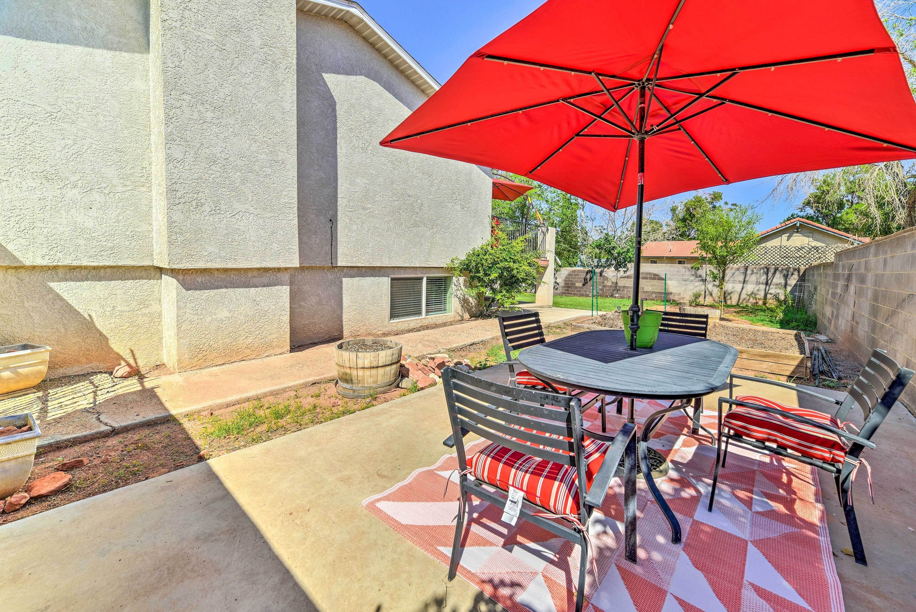 Eine Terrassenausstattung mit rundem Tisch, Stühlen, einem roten Sonnenschirm und einem Feuerkorb.