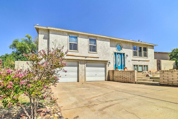 A two-story house with a garage, a blue door, and a small garden with pink flowers. - 1 Mi to Antelope Canyon: 4BR Page Family Home (Page)