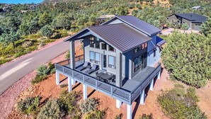 A modern two-story house with a balcony, surrounded by a hilly landscape. - Modern Pine Retreat w/ Deck & Stunning Views! (Pine)