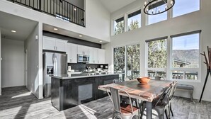 A modern kitchen with a central island, white cabinetry, stainless steel appliances, and large windows offering views of the outdoors. - Modern Pine Retreat w/ Deck & Stunning Views! (Pine)
