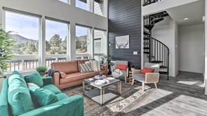 A spacious living room with a high ceiling, large windows, a staircase, and a view of the outdoors. - Modern Pine Retreat w/ Deck & Stunning Views! (Pine)