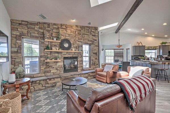 Amplia sala de estar con pared de piedra, muebles de cuero, chimenea y una cocina al fondo.