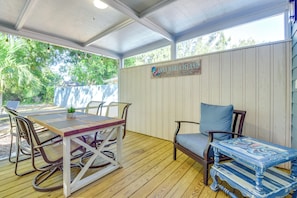 An outdoor patio with a wooden table and chairs, a cushioned bench, and a decorative table with a blue and white pattern. - Charming Vacation Rental: Close to Downtown! (Sarasota)