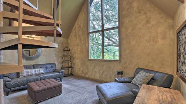A spacious loft bedroom with a large window, a loft bed, a sofa, and a wooden coffee table.