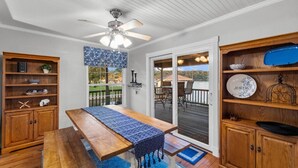 Une table à manger en bois, agrémentée d’un chemin de table bleu, un ventilateur de plafond et une vue sur une terrasse aménagée avec du mobilier d’extérieur.