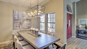 A dining area with a long table, chairs, a hanging light fixture, and artwork on the walls.