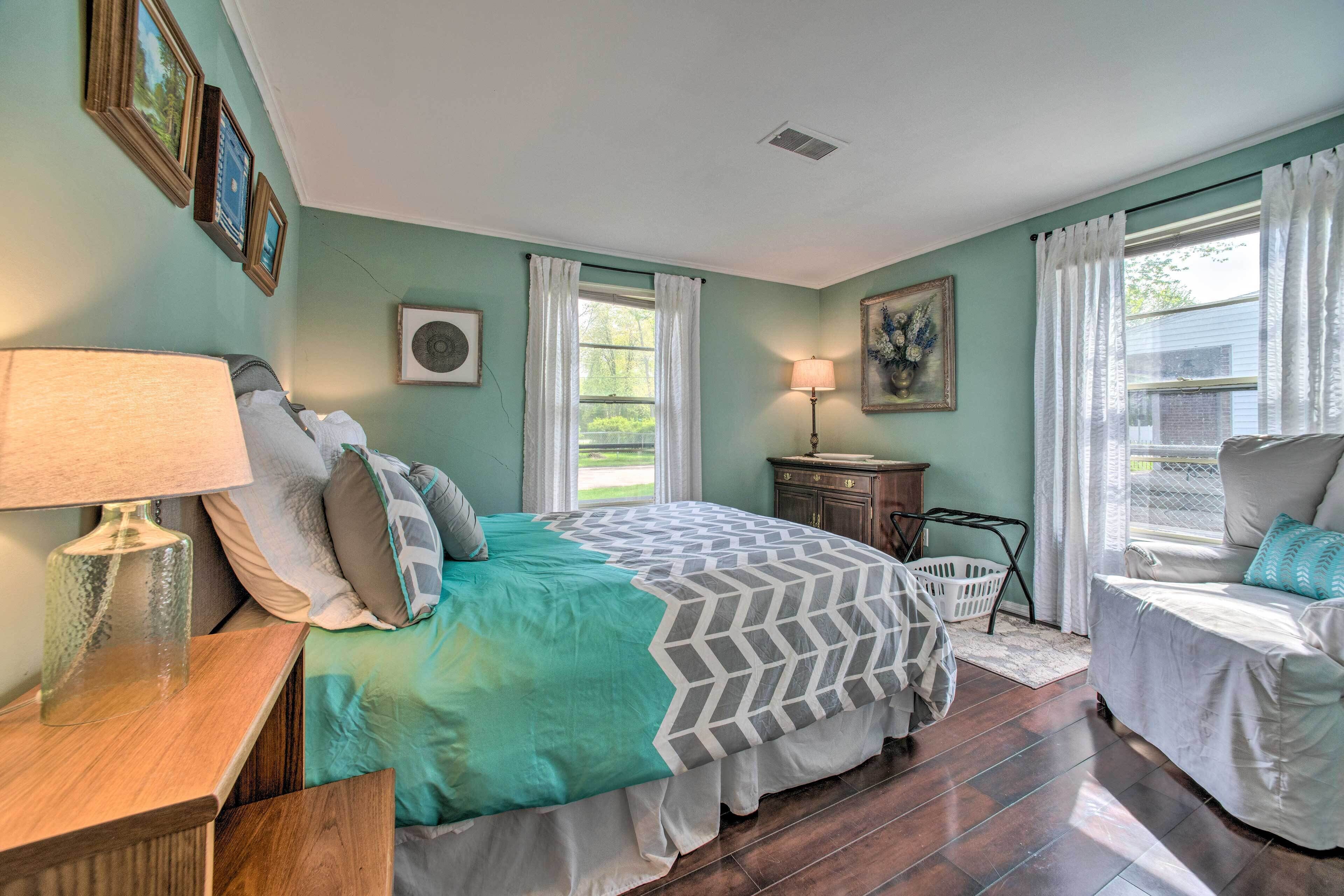 A bedroom with a bed, bedside table, lamp, dresser, and a window with curtains.