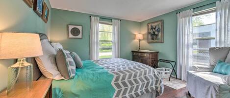 A bedroom with a bed, bedside table, lamp, dresser, and a window with curtains.