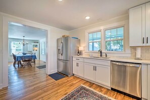 A modern kitchen with stainless steel appliances, white cabinetry, and a dining area with a wooden table and chairs. - Historic Family Home < 1 Mi to Long Beach! (Oak Island)