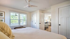 A bedroom with a large bed, white walls, and a ceiling fan. There are white doors leading to other rooms. - Historic Family Home < 1 Mi to Long Beach! (Oak Island)