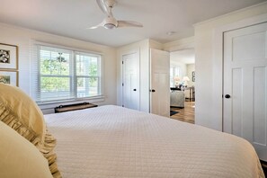 A bedroom with a large bed, white walls, and a ceiling fan. There are white doors leading to other rooms. - Historic Family Home < 1 Mi to Long Beach! (Oak Island)