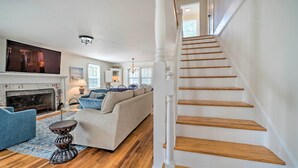 A spacious living room with a fireplace, a staircase, and a large TV. - Historic Family Home < 1 Mi to Long Beach! (Oak Island)