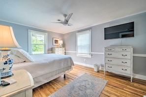 Une chambre à coucher comprenant un lit, une table de chevet, une lampe, une commode, un téléviseur et un ventilateur de plafond.