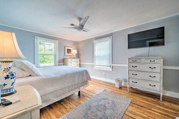 Quarto com cama, mesa de cabeceira, abajur, cômoda, televisão e ventilador de teto.